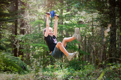 Child enjoying Zip Line Kit 150 Feet With Seat And Carabiner Heavy Duty One Quarter Inch Galvanized Cable Backyard Fun For Families Supports Up To 350 Lbs Weather Resistant Easy Setup For Hours Of Outdoor Adventure in forest.