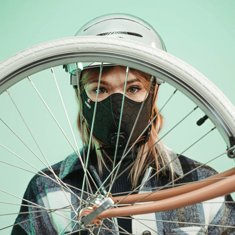 Person wearing Road Ready Nano Light Hexagon Motorcycle Half Face Mask With Anti Pollution Filter under a helmet, holding bicycle wheel.