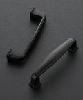 Two matte black cabinet pulls on a textured surface, part of 60 Pack 3 Inch Cabinet Pulls Matte Black for Kitchen Cabinets and Drawers Solid Zinc Alloy Hardware Easy Install Durable Cupboard Handles for a Sleek Modern Kitchen.