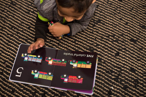 Child reading Totally Rad Toddler Counting Book Featuring Ten Noisy Rickshaws And Hella Fun Indian Culture educational material with colorful trucks.