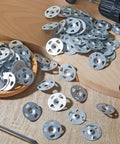Snag This Pro Grade Bulk Pack Of 2000 Galvanized Steel Washers Sized At 1-1/8 Inches, scattered on a wooden surface with a drill.