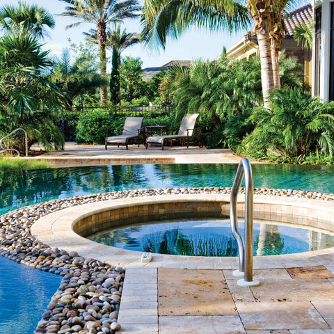 Front view of outdoor pool with circular spa, stone deck, pebble border, and stainless steel handrail