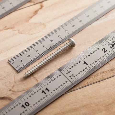 Top view of Beefy Machinist Ruler Set Four Pack Stainless Steel With Six Eight Twelve And Fourteen Inch Lengths around a screw on wood surface