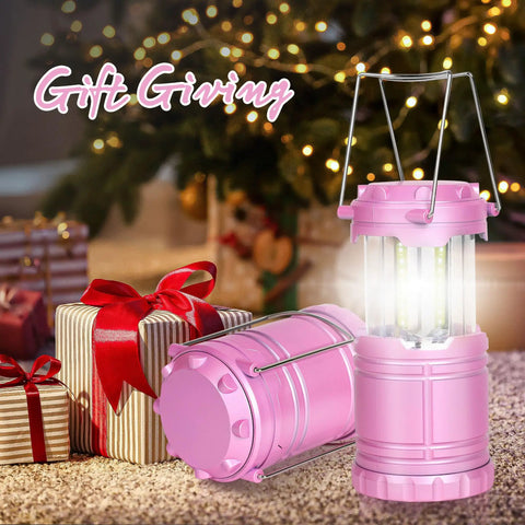 Pink LED Camping Lanterns with Portable Handle next to gift boxes under a decorated Christmas tree, lit with warm glow