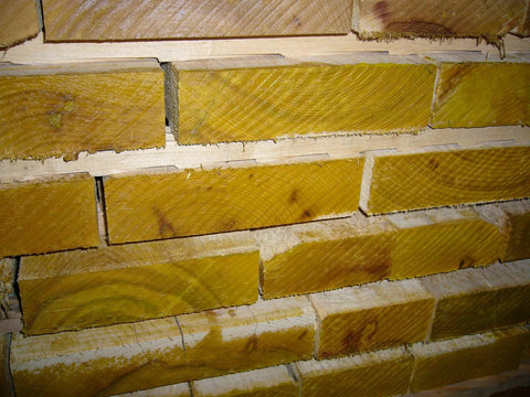 Stacked wooden planks with visible end grain sealer coating, used for logs and lumber to prevent checking during drying.