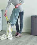 Person emptying laundry into washing machine from Tota Laundry Hamper With Dual Compartments And Lid, 60 Liter Separation Basket With 2 Removable Washing Bags And Handles, Gray, Self Locating Bags For No Fuss Easy Emptying, Perfect For Bedroom, Bathroom Or Utility Room.