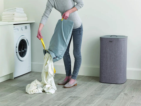 Person emptying laundry into washing machine from Tota Laundry Hamper With Dual Compartments And Lid, 60 Liter Separation Basket With 2 Removable Washing Bags And Handles, Gray, Self Locating Bags For No Fuss Easy Emptying, Perfect For Bedroom, Bathroom Or Utility Room.