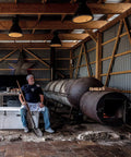 Rugged Rotomolded Outdoor Cooler With Three Inch Insulation And Bear Proof Certification beside a man resting near a large smoker.