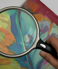 Hand holding Lit 5 Inch Round Magnifier With LED 2X Magnification And 6X Bifocal Lens Ergonomic Handle over colorful paper