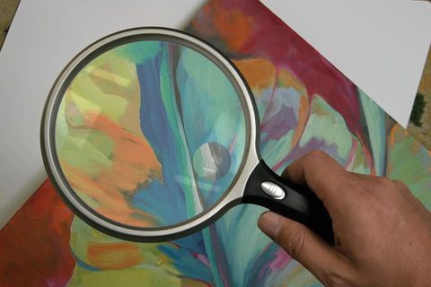 Hand holding Lit 5 Inch Round Magnifier With LED 2X Magnification And 6X Bifocal Lens Ergonomic Handle over colorful paper
