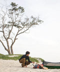 Person setting up Forest Green Hybrid Ground Tent Or Hammock With Strap Bundle For Car Camping And Backpacking on sandy beach.
