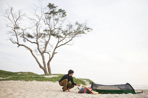 Person setting up Forest Green Hybrid Ground Tent Or Hammock With Strap Bundle For Car Camping And Backpacking on sandy beach.