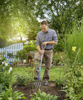Person using Nature Line Spading Fork For Quick, No-Fuss Root-Safe Digging And Loosening Soil In Garden Beds among plants