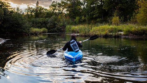 Person kayaking in river with green waterproof backpack 10L 20L 30L 40L with IPX8 phone case for water sports fishing boating kayaking