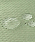 Close-up of water droplets on sage green textured polyester fabric of Sage Green Cloth Shower Curtain Liner With 2 Magnets, Textured Polyester For Spa Like Feel, Soft Hotel Quality Waterproof, Lightweight And Machine Washable, 72x84 Inch.