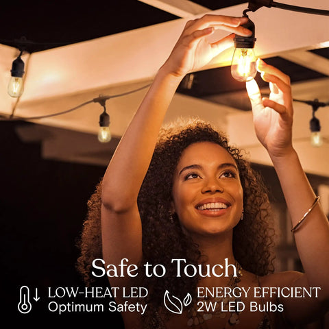 Woman adjusting Ambience Pro Waterproof LED Outdoor String Lights with 2W Vintage Edison Bulbs hanging on a patio.