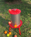 Water-Powered Fruit Wine Press For Home Cider And Natural Juice Making, Electricity-Free Hydraulic Press With 10.7 Gallon Capacity, Includes Filter Bag And Splash Guard, Awesome For Easy DIY Wine, Cider, And Fresh Juice. Outdoor red metal fruit press with apples and oranges