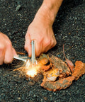 Hands using Magnesium Fire Starter Kit Portable Waterproof Survival Tool For Camping Hiking Bushcraft And Emergency Prep With Built In Flint Serrated Blade And Striker For Easy Sparks In Any Weather to create sparks over kindling.