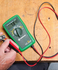 Person using DM-25 CATIII 600V Manual and Auto Ranging Digital Multimeter with Large Easy Read Display on a battery.