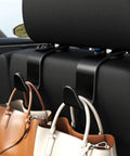 Black S-type car seat headrest hooks mounted on the seat back, holding handbags.