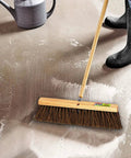 Heavy Duty 18 Inch Palmyra Bristle Push Broom For Garage Indoor Floor Sweep with wooden block on a wet concrete floor.