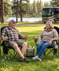 Two people sitting on an Oversized Padded Camping Chair Two Pack Heavy Duty Quad Chair with lumbar support and cup holder outdoors.