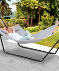 Heavy Duty Hammock Stand For Indoors And Outdoors, 660 Lb Capacity, Fits 9.6 To 14 Ft Hammocks, All Steel Frame, Built To Last Weatherproof Universal 2 Person Ready, Black, with person reclining in backyard