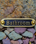 Brass bathroom door sign mounted on stone wall with rustic finish