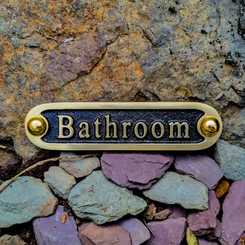 Brass bathroom door sign mounted on stone wall with rustic finish