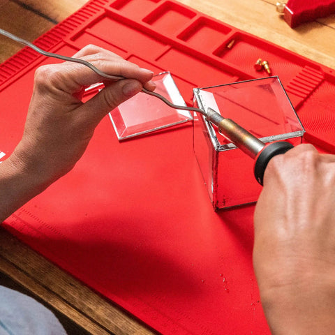 Hands using Power Grip Variable Wattage Soldering Station 20 To 80W With Built-In Safety Rest for electronics on red mat.