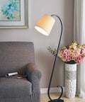 Oil Rubbed Bronze Floor Lamp With Elegant Scroll Design next to a gray sofa, floral vase, and artwork, 55.75 inches tall, 19.5 inches wide