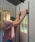 Woman opening window of Desert Sand Outdoor Storage Shed 15x8 Ft Resin Backyard Tool Shed with Lockable Doors inside view