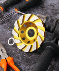 4 Inch Turbo Diamond Grinding Cup Wheel With 12 Segments For Concrete Tile Marble And Rock, Heat Treated Cup Design For Long Life, Ideal For Angle Grinders, 0.86 Inch Arbor, Heavy Duty Grinding On Hard Surfaces on a workbench next to pliers and screwdriver