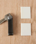 Self-adhesive door corner foam seals in white; two square pads shown with keys on a wooden surface.
