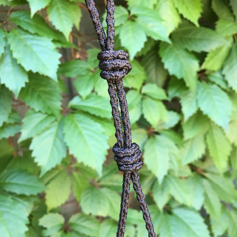 Close-up of 3mm Paracord With Textured Posi Lock Ninja Black Color Made In USA, showing detailed knotting against a leafy background.