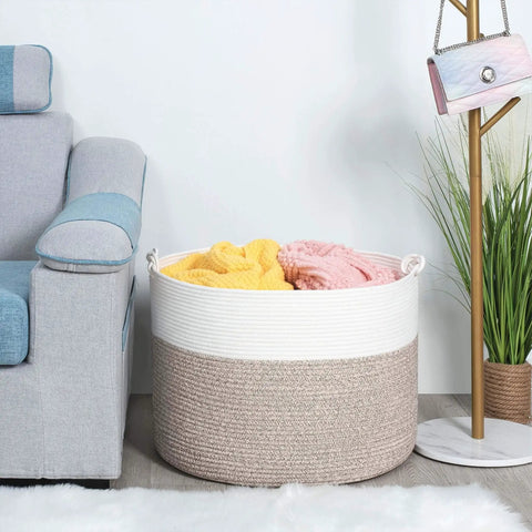Extra Large 22x16 Inch Cotton Rope Storage Basket With Grab Handles next to sofa, filled with colorful blankets, in living room.