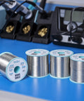 Sn60Pb40 Solder Wire With 2.2% Flux, 0.3 mm Diameter, 100 g Spool displayed with soldering equipment on table.