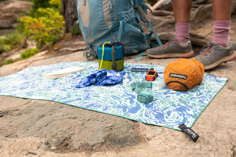 Backpacking gear on a patterned mat featuring a Two Person Camping Mess Kit With Insulated Mugs, Deep Dish Bowls, Folding Sporks.