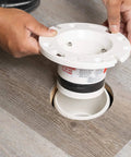 Hand installing Four Inch Closet Flange Replacement For Toilets With Adjustable Compression Joint on brown wood floor