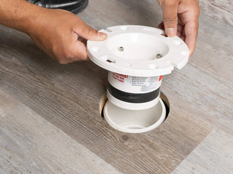 Hand installing Four Inch Closet Flange Replacement For Toilets With Adjustable Compression Joint on brown wood floor