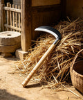 Lightweight Wood Handle Grass Sickle With Carbon Steel Blade For Easy Weeding And Lawn Care resting on straw pile outdoors.