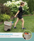 Person pulling Taupe 15.5 Gallon Resin Garden Cart On Wheels Lightweight Two Wheel Wheelbarrow for outdoor garden tasks