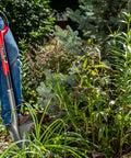 Person using a Heavy Duty Garden Shovel With Serrated Blade For Root Cutting And Digging In Tough Soil, red ergonomic spade in yard.
