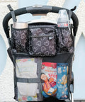 Cups N Cargo Stroller Caddy Organizer With Cup Holder For Any Stroller Universal Fit Durable Mesh Storage Pockets Travel Essential For Parents On The Go Mickey Mouse Black on stroller handle with bottles and mesh pockets filled with items.