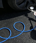 Person using Heavy Duty 1/4 Inch By 100 Ft Air Compressor Hose Rated 300 Psi to inflate a car tire on asphalt.