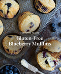 Baked gluten-free blueberry muffins with one sliced, buttered muffin on a rustic surface, showcasing wholesome texture and berries.