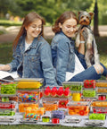 Two people sitting in a park with a dog, surrounded by a 60 piece leak proof food storage set with lids BPA free plastic containers.