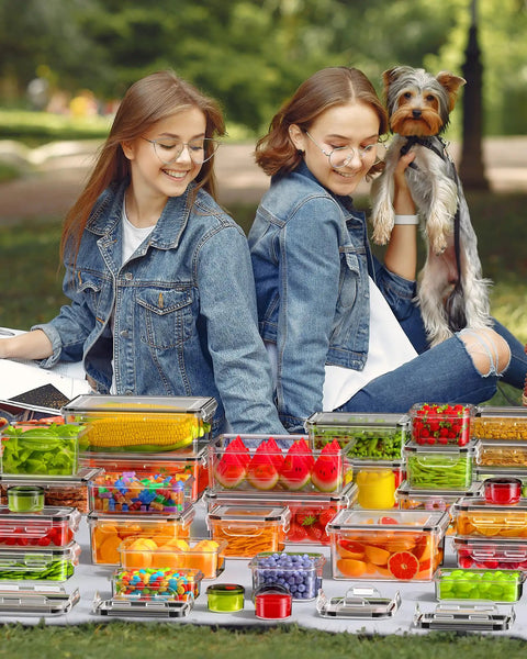 Two people sitting in a park with a dog, surrounded by a 60 piece leak proof food storage set with lids BPA free plastic containers.