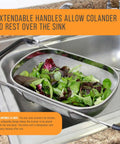 6-Quart Over The Sink Stainless Steel Colander With Expandable Rubber Handles filled with fresh salad, resting above kitchen sink.