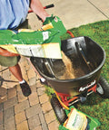 Person pouring seed into Push Broadcast Spreader 130 Lb Hopper Capacity Easy To Use Direct Rod Control 13 Inch Pneumatic Tires